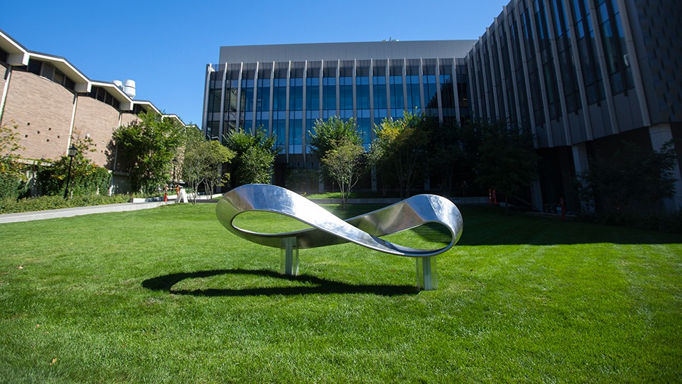 A sculpture resembling a Mobius strip in front of a building.